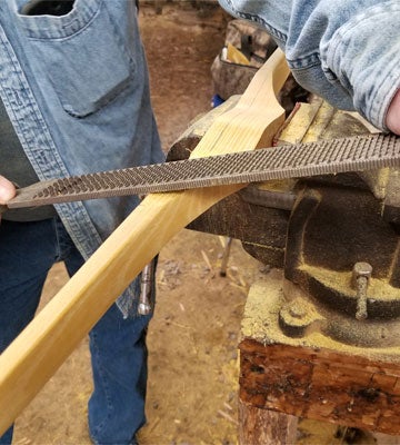 A bow stave in a vice being worked on with a rasp